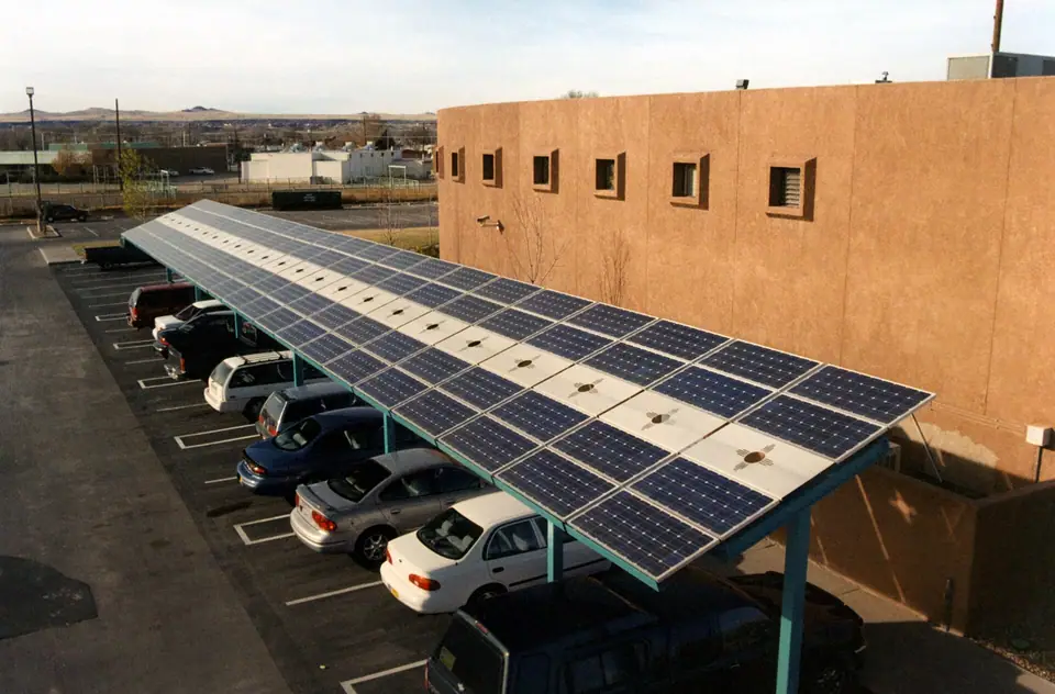 Bir binanın yanındaki açık otoparkta araçların üzerini örten güneş paneli sundurması