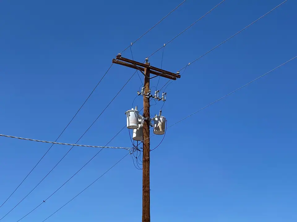 Mavi gökyüzü önünde üzerinde iki küçük dağıtım trafosu bulunan ahşap elektrik direği